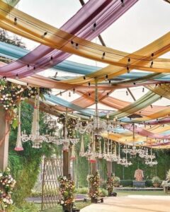 Rustic Bohemian Haldi: Outdoor haldi ceremony with wooden decor elements, vintage rugs, colorful cushions, dreamcatchers, hanging lanterns, and boho floral arrangements, creating a relaxed and earthy atmosphere."